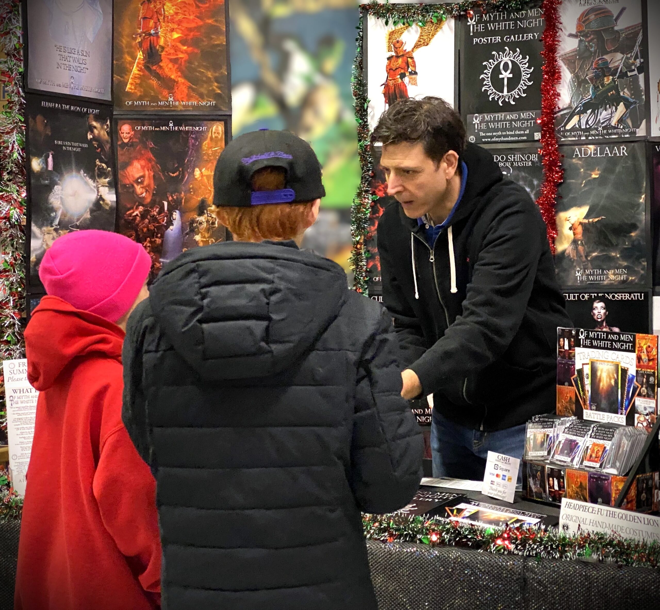 Author Francesco Coscarella standing behind his exhibit speaking with fans at a Christmas event held at Heroes World from Of Myth and Men: The White Night by Francesco Coscarella