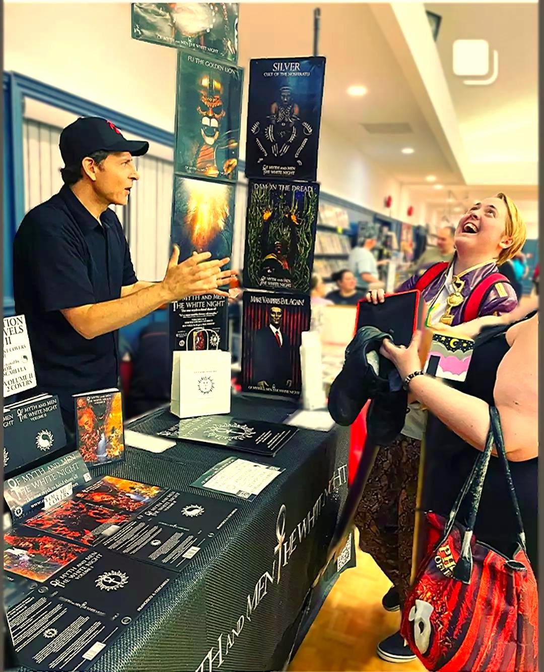 Author Francesco Coscarella standing behind his exhibit speaking with fans at an event from Of Myth and Men: The White Night by Francesco Coscarella