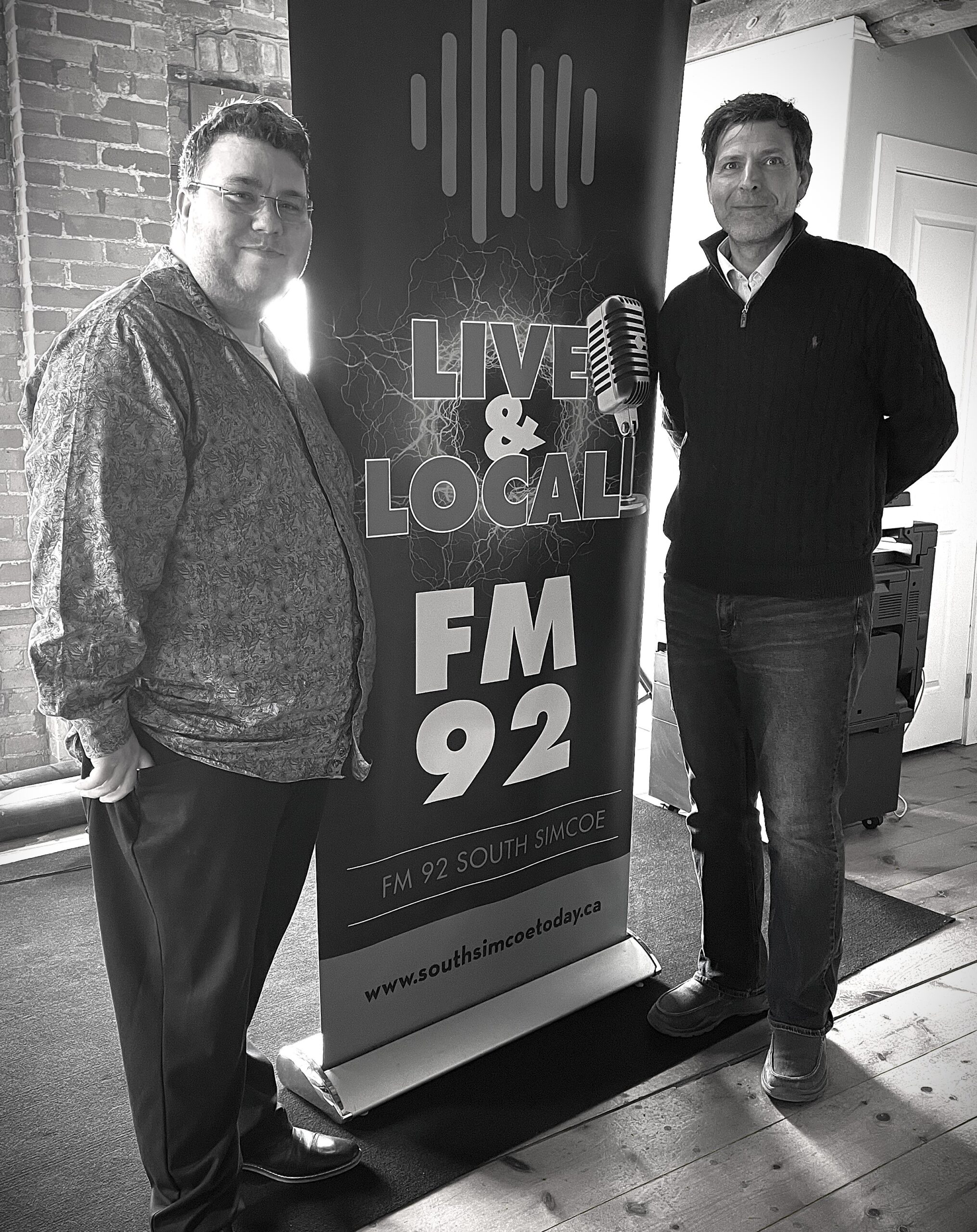 Author Francesco Coscarella standing next to banner for FM 92 South Simcoe with interviewer Devin Merkac from Of Myth and Men: The White Night by Francesco Coscarella